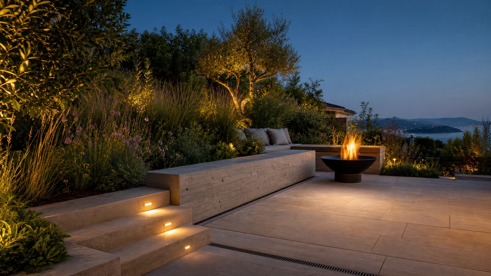 Blue-hour Bay Area terrace with limestone paving, seat wall, step lights, drainage channel, and drought-tolerant planting